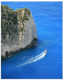 Stretched view of a cliff above the blue sea with a boat sailing along the coast